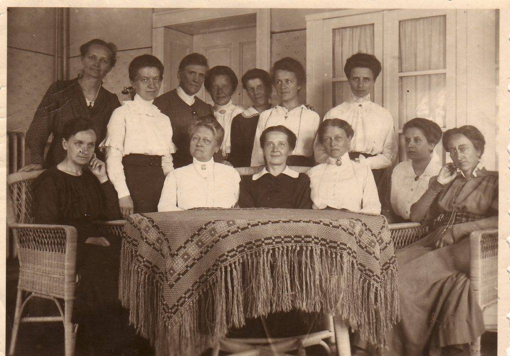 schwarz-weiß Fotografie von Johanna Just (sitzend, zweite von links), umgeben von 12 weiteren Frauen, teils neben ihr um einen Tisch sitzend, teils in zweiter Reihe stehend, Margareta Just ebenfalls sitzend vierte von links um 1926 (Oberstufenzentrum III Potsdam)